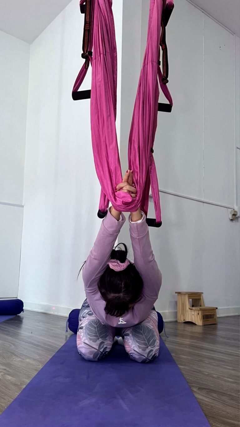 Student stretching forward in aerial yoga hammock at YogaAereo Auckland.